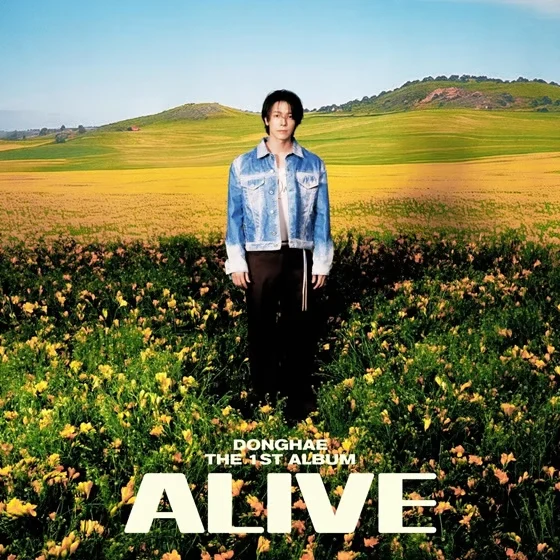 ALIVE album cover — Donghae standing in a field of yellow wildflowers, rolling green hills and blue sky behind him