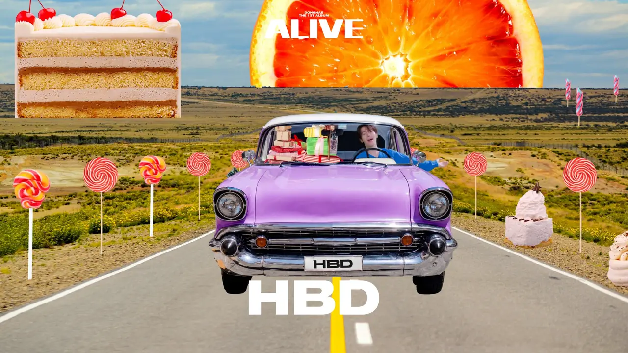 Still from the HBD music video — DONGHAE behind the wheel of a purple convertible with an HBD licence plate, gift boxes piled in the passenger seat, lollipops and a birthday cake lining the desert road under the album's ALIVE wordmark